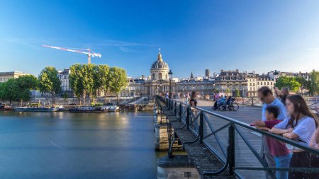 Téléchargez les photos : Les personnes marchant sur le Pont des Arts sur la Seine jusqu'à l'Institut de France intemporel hyperlapsus au coucher du soleil avec ciel bleu - Paris, France - en image libre de droit