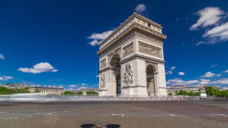 Téléchargez les photos : L'hyperlapsus de l'Arc de Triomphe (Arc de Triomphe de l'Étoile) intemporel avec circulation sur une route circulaire. Célèbre monument à Paris, situé à l'extrémité ouest des Champs-Elysées. Ciel bleu en été - en image libre de droit