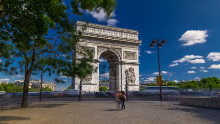 Photo for The Arc de Triomphe (Triumphal Arch of the Star) timelapse hyperlapse with traffic on circle road and trees around. Monument in Paris at the western end of the Champs-Elyseees. Blue cloudy sky - Royalty Free Image