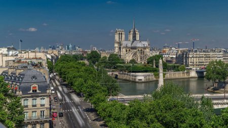 Photo for Cite Island and Cathedral Notre Dame de Paris on the background timelapse from the Arab World Institute observation deck. Top view. Green trees, Seine river, Blue cloudy sky at summer day. France. - Royalty Free Image