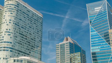 Téléchargez les photos : Des gratte-ciel modernes avec de nombreuses fenêtres intemporelles dans le célèbre quartier financier et d'affaires de Paris - La Défense. Réflexions sur un verre avec des nuages bleus et un ciel bleu le jour d'été - en image libre de droit