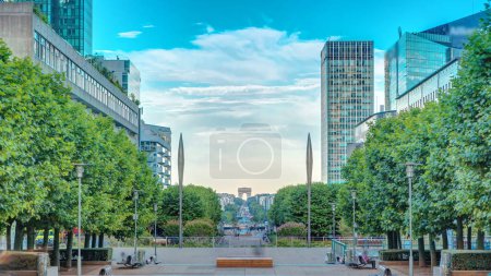 Photo for Skyscrapers of La Defense timelapse - Modern business and residential area in Paris, France. Arc de Triomphe with Champs Elysees on background. Green trees, blue cloudy sky at evening - Royalty Free Image