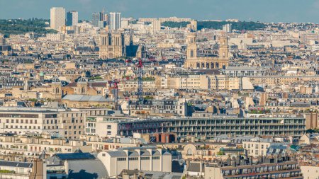 Téléchargez les photos : Panorama aérien au-dessus des toits des maisons dans un timelapse parisien. Vue du soir sur Notre Dame de Paris et Saint-Sulpice avant le coucher du soleil. Grues sur un chantier - en image libre de droit