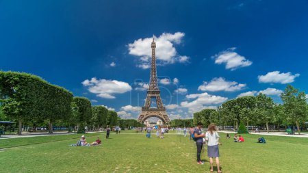 Photo for Eiffel Tower on Champs de Mars in Paris timelapse hyperlapse, France. Blue cloudy sky at summer day with green lawn and people walking around. Moving forward - Royalty Free Image