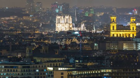 Foto de El panorama aéreo sobre los tejados de las casas en un timelapse de la noche de París. Vista superior con la iluminada catedral de Notre Dame de París y Saint-Sulpice. Luces apagadas - Imagen libre de derechos