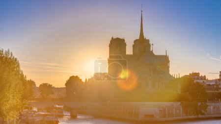 Téléchargez les photos : Vue arrière de la cathédrale Notre Dame de Paris au coucher du soleil avec soleil dans le cadre intemporel. Vue depuis le pont Tournelle. Ciel orange en arrière-plan. Paris, France, Europe. - en image libre de droit