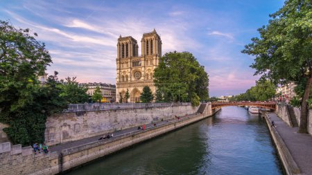 Foto de Vista frontal de la catedral iluminada de Notre Dame De Paris día a noche. Vista desde el puente del cardenal Lustiger. Cielo colorido sobre un fondo. París, Francia, Europa. - Imagen libre de derechos