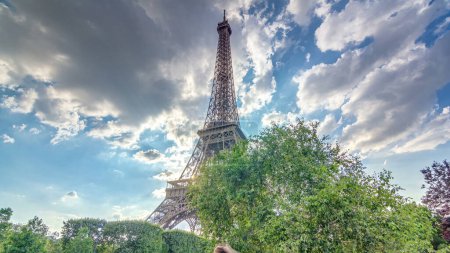 Photo for Sun behind the Eiffel tower with warm rays of light in clouds during sunset timelapse hyperlapse. It is one of the most recognizable landmarks in the world. Blue cloudy sky at sunny evening - Royalty Free Image