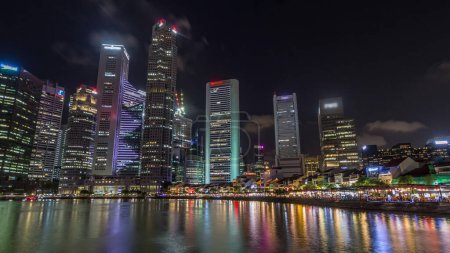 Téléchargez les photos : Quai de Singapour avec de grands gratte-ciel dans le quartier central des affaires et de petits restaurants sur Boat Quay nuit timelapse hyperlapse. Tours reflétées dans l'eau - en image libre de droit