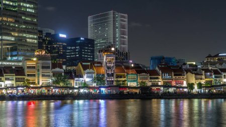 Foto de Singapur muelle con restaurantes de centro comercial y rascacielos altos en el distrito central de negocios en Boat Quay noche timelapse hiperlapso. Casas reflejadas en el agua - Imagen libre de derechos