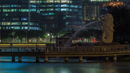 Téléchargez les photos : La fontaine Merlion et Singapour skyline nuit. Des gratte-ciels sur fond. Merlion est une créature imaginaire avec une tête de lion et le corps d'un poisson et est souvent considéré comme un symbole de Singapour. - en image libre de droit