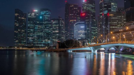 Photo for Esplanade bridge and downtown core skyscrapers in the background Singapore night to day transition timelapse. Illuminated towers reflected in water - Royalty Free Image