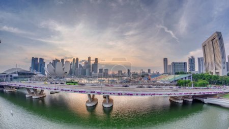 Téléchargez les photos : Vue aérienne du coucher du soleil sur le pont Helix et Bayfront Avenue avec la circulation timelapse à Marina Bay d'en haut avec gratte-ciel skyline sur un fond, Singapour. Stade flottant sur la droite - en image libre de droit