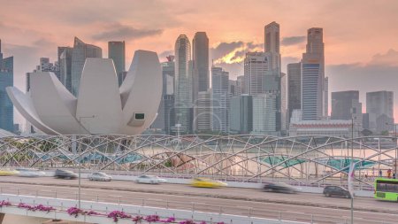Téléchargez les photos : Vue aérienne du coucher du soleil sur le pont Helix et Bayfront Avenue avec la circulation timelapse à Marina Bay d'en haut avec gratte-ciel skyline sur un fond, Singapour. Ciel orange - en image libre de droit