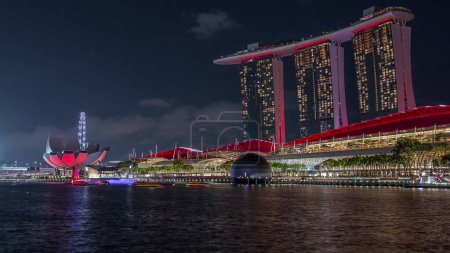 Foto de Hermoso espectáculo de láser y fuente musical en el paseo marítimo de Marina Bay Sands en Singapur noche timelapse. Multitud de espectadores mirando detrás de él. Barcos flotando alrededor - Imagen libre de derechos