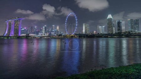Téléchargez les photos : Skyline du centre-ville de Singapour vue de l'autre côté de l'eau de The Garden East nuit timelapse. Singapour. Réflexion dans l'eau avec des gratte-ciel éclairés - en image libre de droit