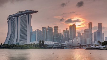 Foto de Puesta de sol sobre el horizonte del centro de Singapur visto desde el otro lado del agua desde The Garden East timelapse. Sol detrás de rascacielos. Singapur. Reflexión en el agua - Imagen libre de derechos