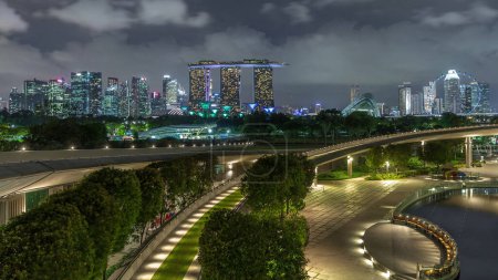 Téléchargez les photos : Vue aérienne Ville de Singapour skyline avec fontaine colorée à Marina barrage jardin nuit timelapse hyperlapse. Marina barrage a une grande fontaine dans le centre et une allée courbe menant au jardin. - en image libre de droit