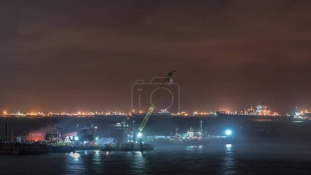 Téléchargez les photos : Marina Barrage de Singapour avec des cargos en attente d'entrer dans l'un des ports les plus fréquentés du monde la nuit timelapse, Singapour. Chargement avec grues, chantier de construction - en image libre de droit