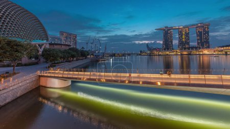 Téléchargez les photos : Skyline dans la baie de Marina avec les théâtres de l'Esplanade sur la baie et la passerelle de l'Esplanade nuit à jour passage timelapse à Singapour avant le lever du soleil. Gratte-ciels réfléchis dans l'eau - en image libre de droit
