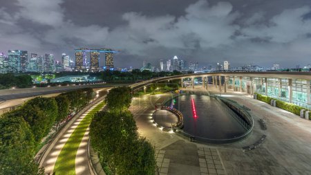 Foto de Vista aérea de Singapur horizonte de la ciudad con colorida fuente en Marina bombardeo jardín noche timelapse. Marina bombardeo tiene una gran fuente en el centro y la curva de la pasarela conduce al jardín. - Imagen libre de derechos