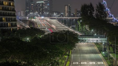 Téléchargez les photos : Trafic avec des voitures sur une rue et et un pont dans le quartier de la baie de la marina de Singapour timelapse de nuit aérienne avec des gratte-ciel sur un fond - en image libre de droit