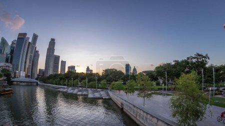 Téléchargez les photos : Les gratte-ciel de Singapour s'alignent avec le pont Anderson blanc et quelques tours du quartier financier près du parc de l'esplanade de jour comme de nuit. Quelques feuillages verts des deux côtés. - en image libre de droit