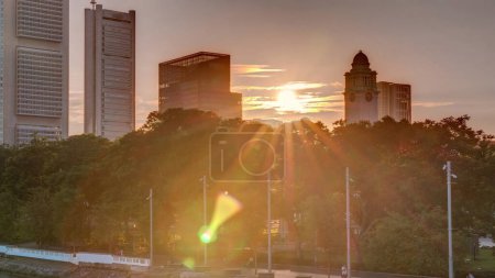 Téléchargez les photos : Coucher de soleil sur Singapour gratte-ciel skyline avec Anderson Bridge blanc et quelques tours de quartier financier près de l'esplanade parc timelapse. Quelques feuillages verts des deux côtés. - en image libre de droit