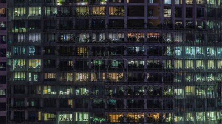 Téléchargez les photos : Immeuble de bureaux moderne avec de grandes fenêtres la nuit timelapse vue rapprochée, dans les fenêtres luisant la lumière brille et certaines personnes à l'intérieur, Singapour - en image libre de droit