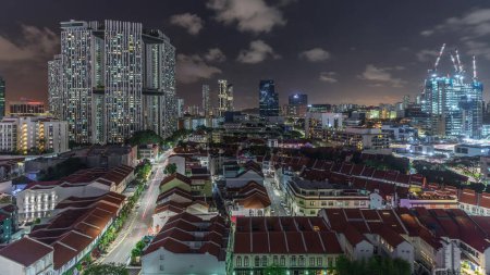Téléchargez les photos : Vue aérienne de Chinatown avec des toits rouges et des gratte-ciel éclairés du Central Business District timelapse, Singapour. Contraste entre bâtiments anciens et modernes. Trafic dans les rues - en image libre de droit