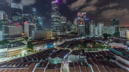 Foto de Vista aérea de Chinatown con techos rojos y rascacielos iluminados del Distrito Central de Negocios timelapse, Singapur. Contraste entre edificios antiguos y modernos. Tráfico en las calles - Imagen libre de derechos