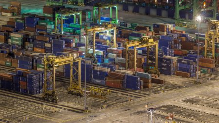 Téléchargez les photos : Port commercial de Singapour timelapse de nuit. Vue rapprochée du port de fret asiatique le plus achalandé avec des centaines de chargeuses qui transportent des marchandises d'exportation et d'importation et des milliers de conteneurs dans le port - en image libre de droit