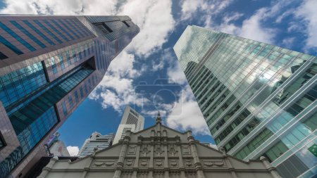 Foto de Mirando hacia arriba la perspectiva de los rascacielos de negocios modernos de vidrio y vista al cielo paisaje de edificio comercial en el timelapse de la ciudad central. Torres con reflejos en Singapur - Imagen libre de derechos