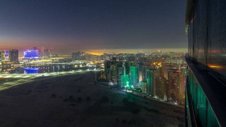 Photo for Abu Dhabi city skyline with illuminated skyscrapers before sunrise from above night to day transition timelapse. Aerial view at foggy morning from rooftop with reflection from glass surface - Royalty Free Image