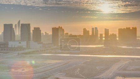 Foto de Rascacielos en Al Reem y Al Maryah Island en Abu Dhabi al atardecer timelapse desde arriba. Paisaje urbano aéreo de Al Reem Island con edificios modernos. Cielo naranja - Imagen libre de derechos