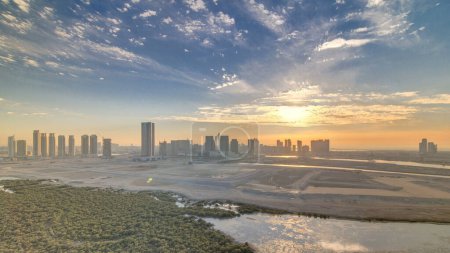 Rascacielos en Al Reem y Al Maryah Island en Abu Dhabi al atardecer timelapse desde arriba. Paisaje urbano aéreo de Al Reem Island con edificios modernos. Cielo naranja