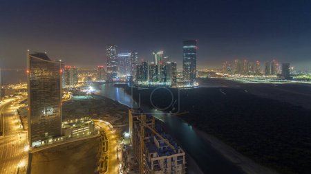 Foto de Rascacielos en Al Reem y Al Maryah Island en Abu Dhabi durante la noche timelapse desde arriba. Paisaje urbano aéreo de Al Reem Island con edificios iluminados con ventanas parpadeantes. Tráfico en la carretera - Imagen libre de derechos