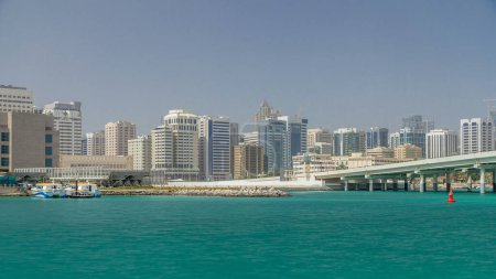 Foto de Edificios modernos en Abu Dhabi horizonte timelapse con centro comercial y playa. Vista desde el paseo marítimo de la isla Al Maryah con reflejos en el agua - Imagen libre de derechos