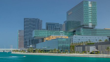 Foto de Edificios modernos de Al Maryah Island en Abu Dhabi horizonte timelapse con centro comercial y paseo marítimo. Vista desde el puente con reflejos de rascacielos en el agua - Imagen libre de derechos