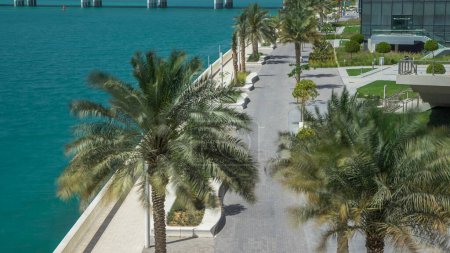 Photo for Walkway of Al Maryah Island in Abu Dhabi timelapse with with palms on promenade. View from the bridge with reflections in water - Royalty Free Image