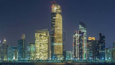 Foto de Vista panorámica del horizonte de Abu Dhabi y frente al mar por la noche timelapse, Emiratos Árabes Unidos. Vista de Corniche con rascacielos iluminados - Imagen libre de derechos