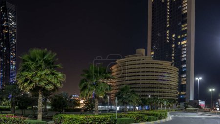 Téléchargez les photos : Les gratte-ciel d'Abu Dhabi illuminés la nuit avec les bâtiments Etihad Towers timelapse. Palmiers dans le parc avec la circulation sur la route. Émirats arabes unis - en image libre de droit