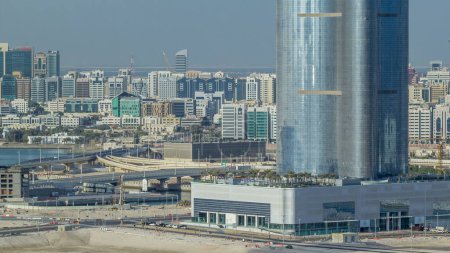 Foto de Edificios en Al Reem y Al Maryah Island en Abu Dhabi timelapse desde arriba. Paisaje urbano aéreo desde la isla Al Reem por la mañana, mostrando la reflexión sobre los edificios y el tráfico en el puente. - Imagen libre de derechos