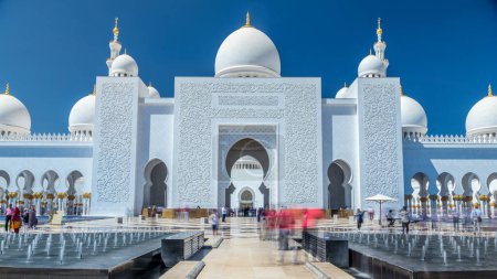 Photo for Sheikh Zayed Grand Mosque timelapse in Abu Dhabi, the capital city of United Arab Emirates. Front view with fountains. Blue sky at sunny day - Royalty Free Image