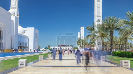Téléchargez les photos : Timelapse de la Grande Mosquée Cheikh Zayed à Abu Dhabi, la capitale des Émirats arabes unis. Les gens marchent dans l'allée. Ciel bleu au soleil - en image libre de droit