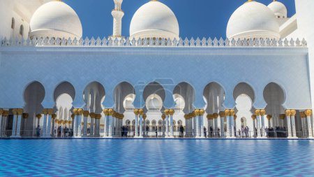 Photo for Sheikh Zayed Grand Mosque timelapse in Abu Dhabi, the capital city of United Arab Emirates. Side view with reflection in water pool. Blue sky at sunny day - Royalty Free Image