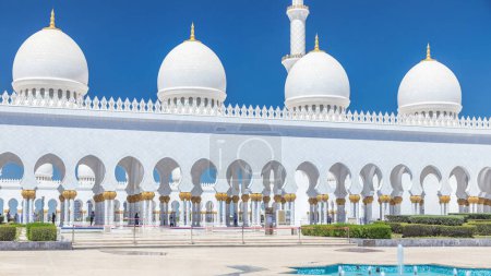 Photo for Sheikh Zayed Grand Mosque timelapse in Abu Dhabi, the capital city of United Arab Emirates. Side view with fountains. Blue sky at sunny day - Royalty Free Image