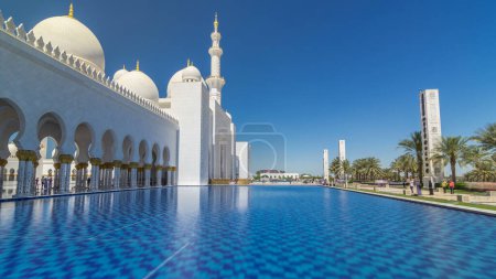 Foto de Sheikh Zayed Gran Mezquita timelapse hiperlapso en Abu Dhabi, la capital de los Emiratos Árabes Unidos. Vista lateral con reflejo en piscina de agua. Cielo azul en el día soleado - Imagen libre de derechos