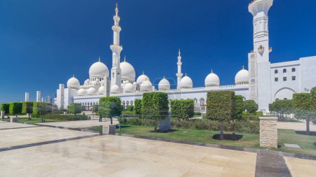 Sheikh Zayed Grand Mosque timelapse hyperlapse in Abu Dhabi, the capital city of United Arab Emirates. Side view with domes and minarets. Trees on foreground. Blue sky at sunny day magic mug #707666644