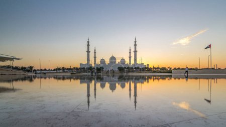 Foto de Sheikh Zayed Gran Mezquita en Abu Dhabi día a noche timelapse transición después de la puesta del sol, Emiratos Árabes Unidos. Vista nocturna desde Wahat Al Karama con reflexiones sobre el agua - Imagen libre de derechos